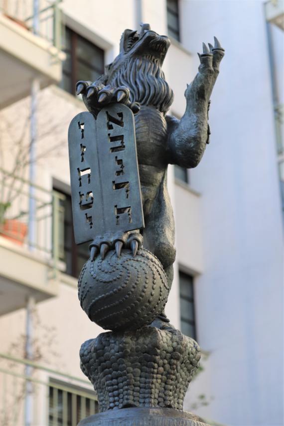 Statue of a standing lion. With one hind leg he stands on a ball and with his claws he holds the covenant tablets.