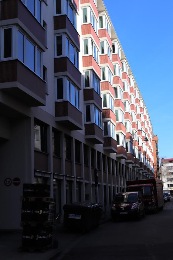 Photo of a residential building. Cars are parked in front of the building.