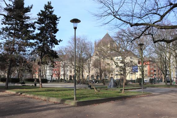 Square with trees and small green area.in the background are buildings.