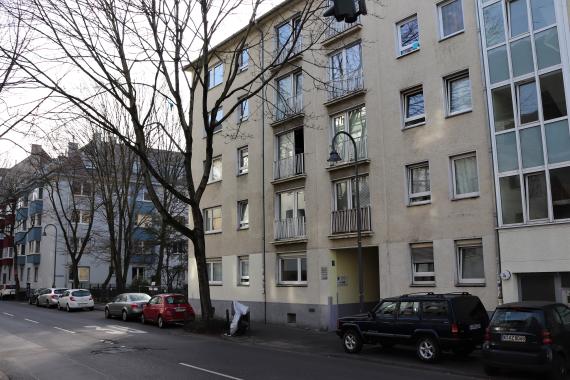 Photo of a normal street with parked cars and residential buildings.