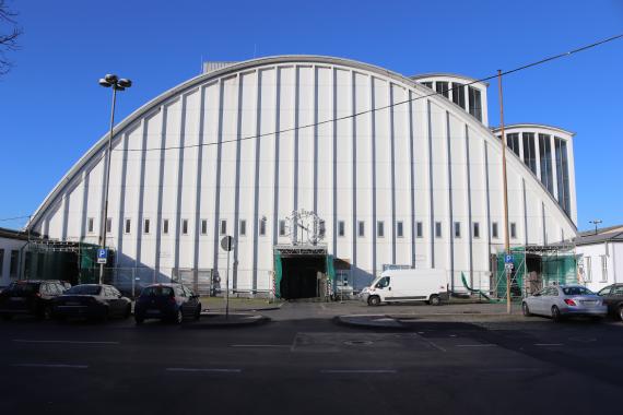 Photo of a large semicircular building with parking lot and cars.