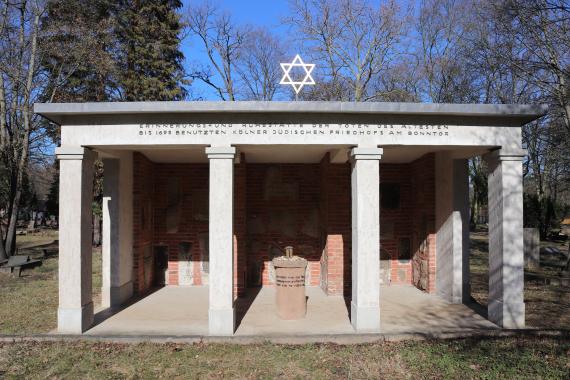 Open structure made of stone. There are tombstones built into the walls and a Star of David on the roof.