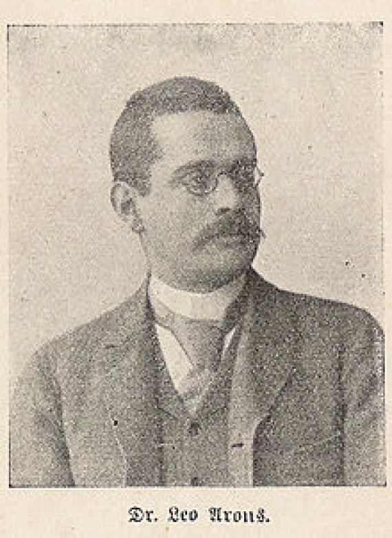 Old portrait of a man with his head turned to the right. He wears glasses and has a mustache.