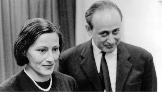 b/w photo, woman on the left in the foreground with a pearl necklace, behind her a man with a high hairline