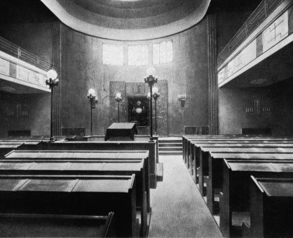 View into a synagogue with rows of benches and galleries. In the background the lectern and the Torah shrine