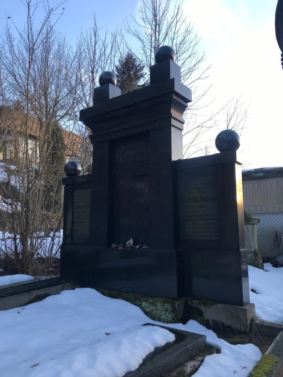 The picture shows Gerson and Jeanette Simson's tombstone, which consists of three elements: two flank elements, of which the left element is dedicated to Gerson and the right element to Jeanette, enclose central element, on which "Gerson Simson" is read once again. On the upper edges there are a total of four spheres, two of them are also supported by ashlars.