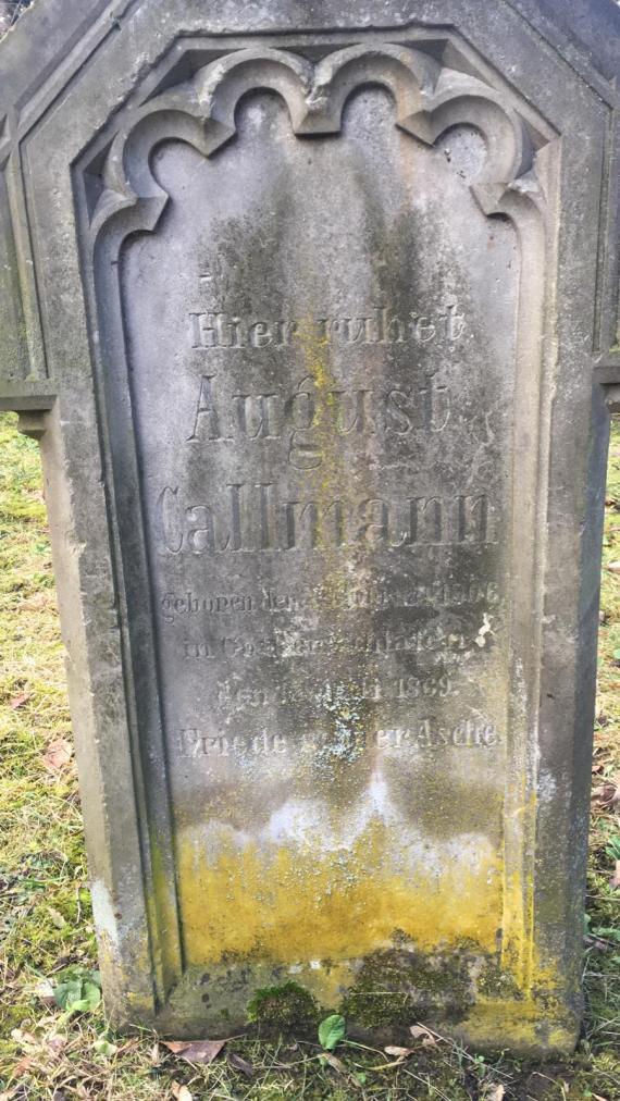 The photo shows a large gravestone with the inscription of the deceased August Callmann including his life data. The stone shows its age through discoloration and wear.