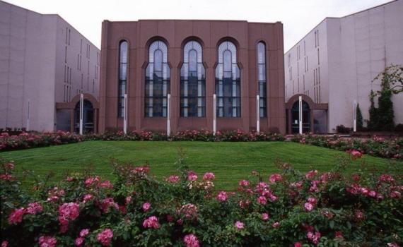 Das Foto zeigt einen Rasenplatz mit Blumenschmuck. Im Hintergrund die Synagoge in F 3, ein kubisches Gebäude mit fünf sakral anmutenden Rundbogenfenstern, flankiert von den beiden Eingängen