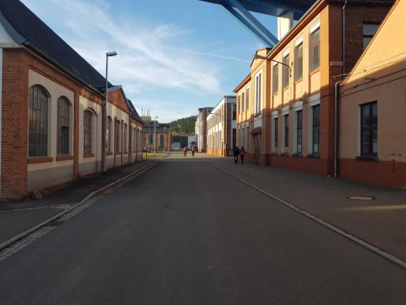 The photograph shows the view into the Simson industrial park. On the left and right side of the Gewerbestraße are production buildings that were already operated by the Simsons and are today either empty or used by various companies.