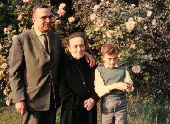 Clara Spaleck mit Sohn Siegfried Spaleck Zu sehen sind drei Personen, die vor einer blühenden Hecke stehen. In der Mitte steht Frau Clara Spaleck (in betagtem Alter, schwarzes Kleid), links steht ihr Sohn Siegfried Spaleck (hellbrauner Anzug) und rechts ein kleiner Junge (weißes Hemd mit grünem Pullunder).