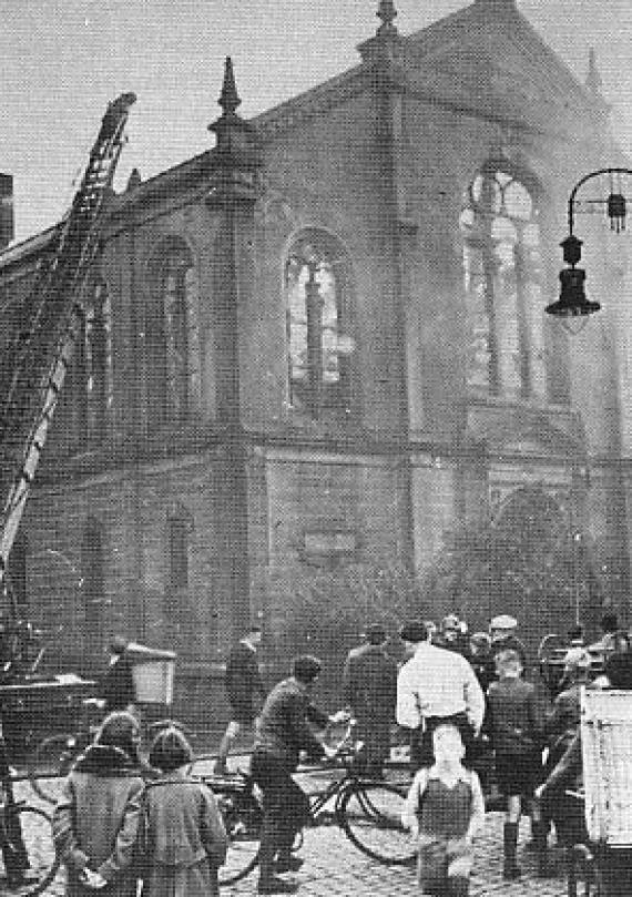 Destroyed synagogue with smoke and many people watching
