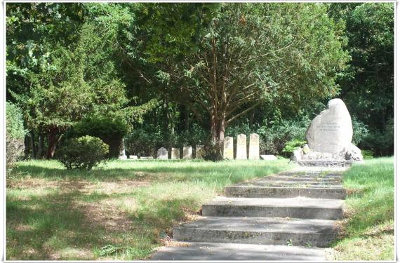 Trees, meadow. On the meadow several gravestones and a large memorial stone.