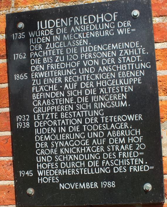 A wall of red bricks. A black board with the data of the cemetery.