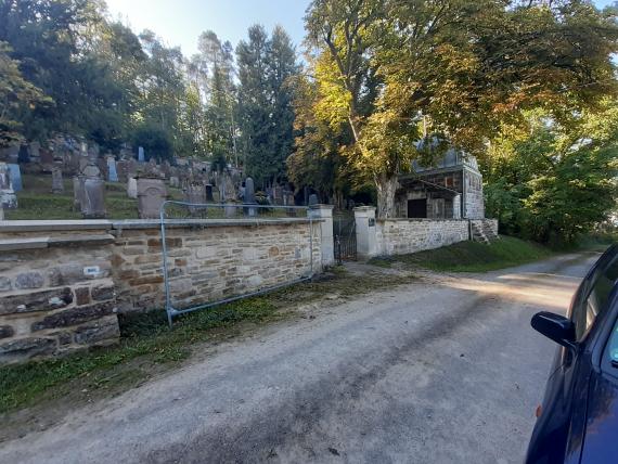 View over the cemetery wall to the entrance gate and the cemetery hall. Next to the gate a barrier grid is visible.