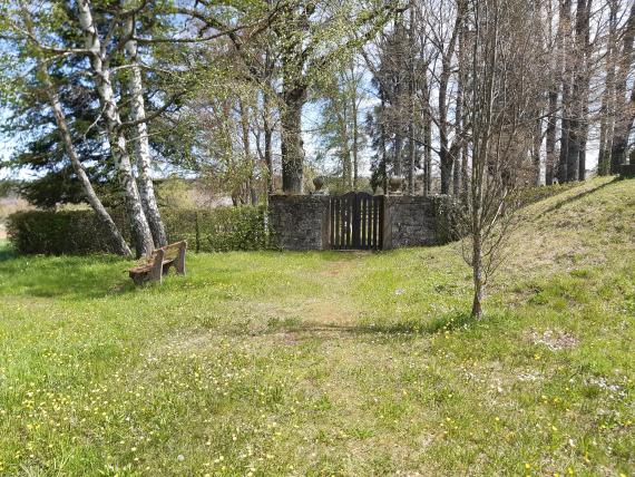 The entrance gate is a simple wooden gate. The two wings are somewhat chest high are located between two short pieces of wall. The rest of the cemetery is surrounded by a wire mesh fence.