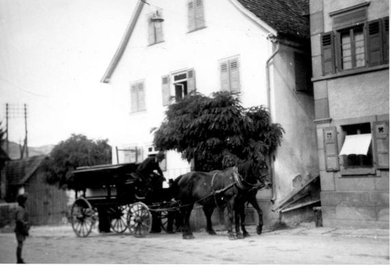 Das Bild zeigt das Wohnhaus gehörte dem Gemeindevorsteher und Immobilienmakler Salomon Pfeiffer. Er, seine Frau und eine Tochter wurden 1941/42 deportiert und ermordet.
Vor dem Gebäude sieht man den Totenwagen der jüdischen Gemeinde. Mit ihm wurden die Verstorbenen zum Friedhof auf dem Schaalberg gefahren.