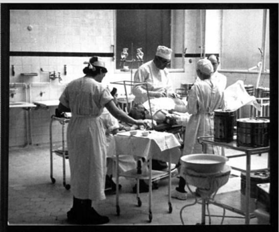 Black and white photograph of three doctors and a nurse performing surgery in the operating room.