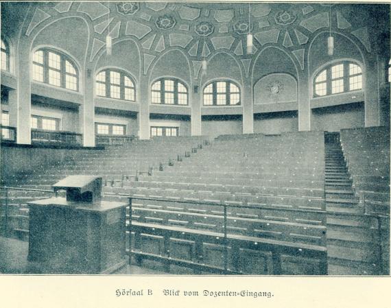 View from the lecturer's desk to the rows of seats in lecture hall B. A dome-shaped room. Lecture hall B is on the upper floor of the main building). The ceiling is decorated with highlights, thin lamps hang down from it. On the walls is a row of oval-shaped windows. Below them are angular windows.