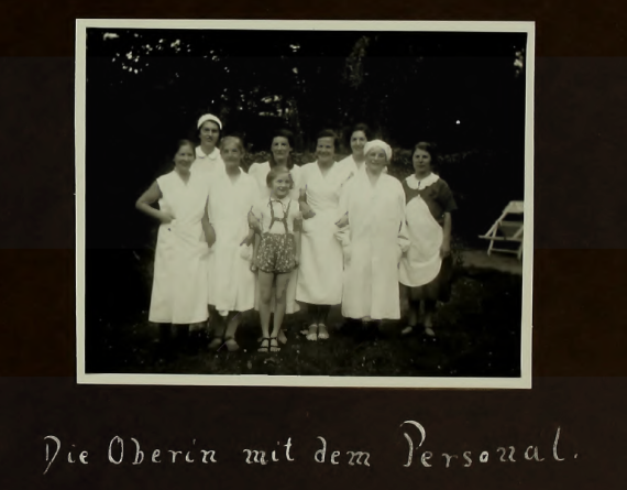 Eight women in work clothes stand together with a girl in the garden.