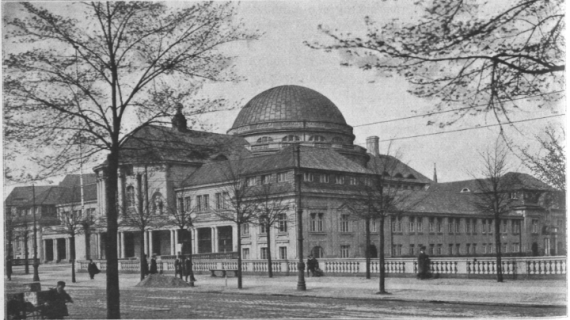 Außenansicht und historisches Foto des Vorlesungsgebäudes der Universität Hamburg. Im Vordergrund eine Allee, wo einige Menschen lang laufen. Das Vorlesungsgebäude ist ein imposantes Gebäude mit einem Kuppeldach in der Mitte. Jede der vier Seiten des Gebäudes ist größer und verbunden mit einem kleineren gangartigen Gebäudeteil. Vorne ist der Eingangsbereich des Gebäudes, der mit nachempfundenen antiken Säulen gesäumt ist.