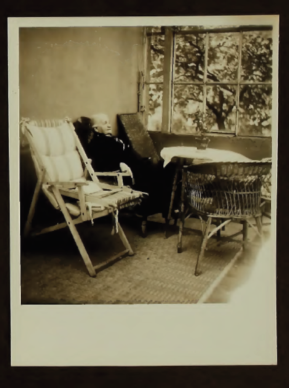 A resident sits comfortably on a chair by a large window with a view of the greenery.