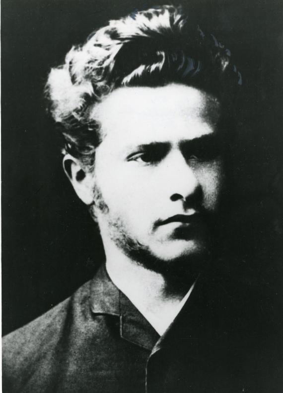 Leo Jogiches Halbportrait in schwarz-weiß. Ein junger Mann schaut nach rechts. Das Gesicht liegt im Halbschatten. Der Blick ist nachdenklich. Die Haare stehen wild vom Kopf ab.