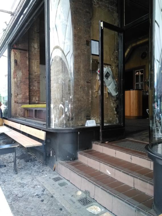 Man sieht den Eingangsbereich des Cafés Luzia. Man sieht große Fenster und hohe Säulen und viele Sitzplätze, außerdem sieht man die Tür zum Cafe.




