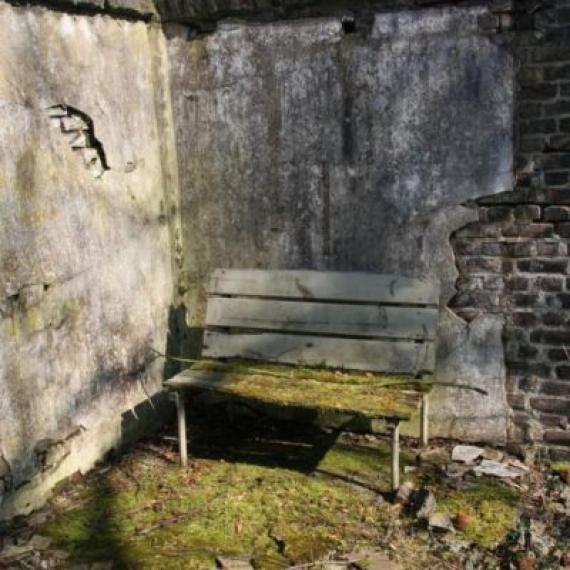 Auf dem Friedhof A corner of a wall. Daroin a bench.