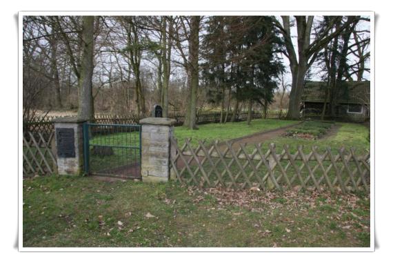 An iron gate between two pillars with wall. Behind it the cemetery