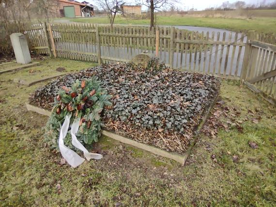 Ein viereckiges Grab, Efeu, geschmückt mit einem Kranz mit Schleifen. Erinnerung an den Auschwitz Erinnerungstag.