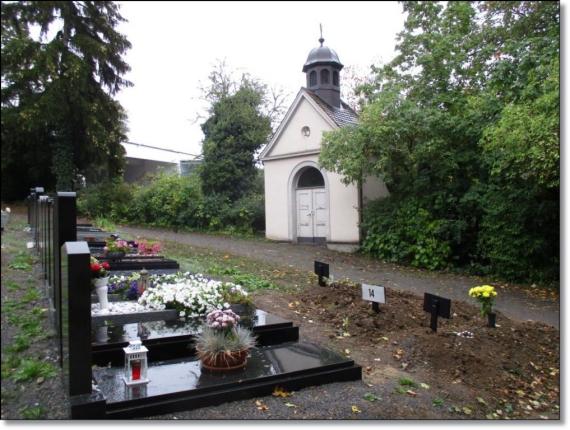 Im Vordergrund ein Feld mit Grabsteinen. Rechts am Rand ein kleineres Gebäude, kapellenartig mit Kuppel