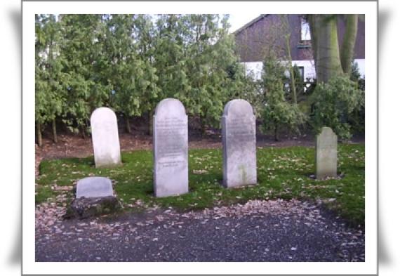 Five tombstones of different sizes. Standing on a lawn. Dainter a fence, bushes.