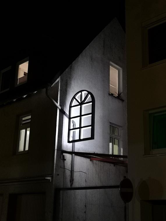 At the former synagogue Lippstadt in the dark you can see a window made of light. It is a work of art. A light installation by the artist Lynne Leegte from Amsterdam. A window of the synagogue is recreated from light.