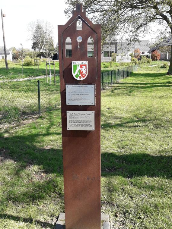 Die Stele aus rostbraunem Metall befindet sich im Eingangsbereich des Friedhofs auf der linken Seite. Sie ist sehr schmal und läuft nach oben dreieckig zu. Ihr Kopfende ist nach dem Vorbild der Fassade der Hülchrather Synagoge gestaltet. Unterhalb des Giebels ist die Plakette angebracht, die den Friedhof als Denkmal ausweist. Darunter befinden sich zwei Informationstafeln, die die Kontexte jüdischer Friedhöfe sowie die Geschichte des jüdischen Friedhofs in Hülchrath erläutern. 