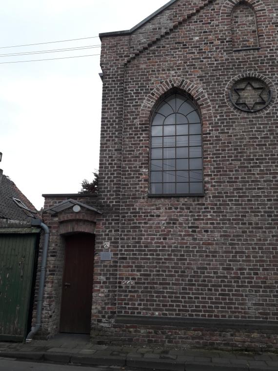 The entrance door is made of dark brown wood and is located in a separate brick door arch on the left side of the building. The building is two stories high and made of dark brown brick. The two pointed windows of the facade are placed quite high up to protect the interior from encroachment. Between them, in the upper third of the facade, a Star of David is embedded in the brickwork.