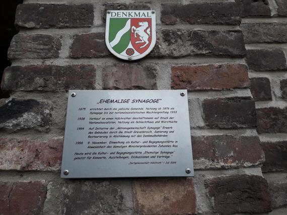 Next to the entrance door of the synagogue there is the plaque that designates the building as a monument, as well as an information board explaining the history of the building, placed by the village community.