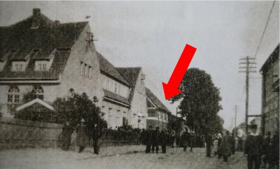 Busy street, on the left in the foreground a large two-story school building with two gable ends facing the street and a longitudinal building connecting them. Behind the large building you can see next the street side of the synagogue.