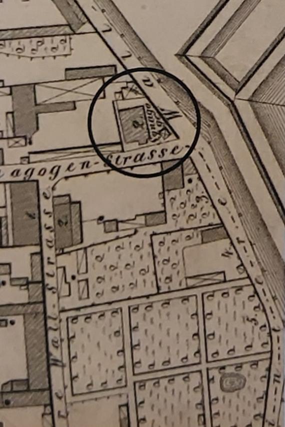 An old city pan painted in ink, on a corner lot of a street mouth you can see a hatched ground plan with the word synagogue.