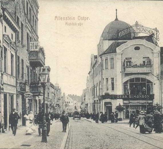 Belebte Strasse mit Strassenbahngleisen, auf der rechten Seite ein Haus mit Kuppel und sehr großer Beschriftung "Gebrüder Simonson"