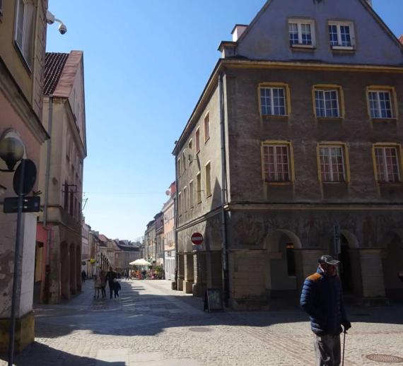 Blick auf eine Strasse in der Altstadt, rechts ein Haus mit Bögen im Erdgeschoß, 5 Etagen mit Giebeldach