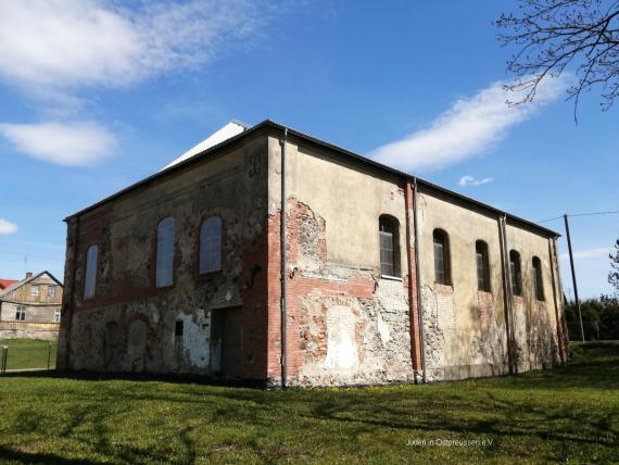 Gebäude mit Rasen im Vordergrund, Spuren von veränderten Fensteröffnungen und abgerissenen Anbau am Verputz erkennbar.