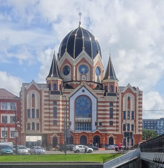 Front of the reconstructed synagogue, with yellowish tones, a large dome in the center and two attached small towers, a large glass rosette in the center.