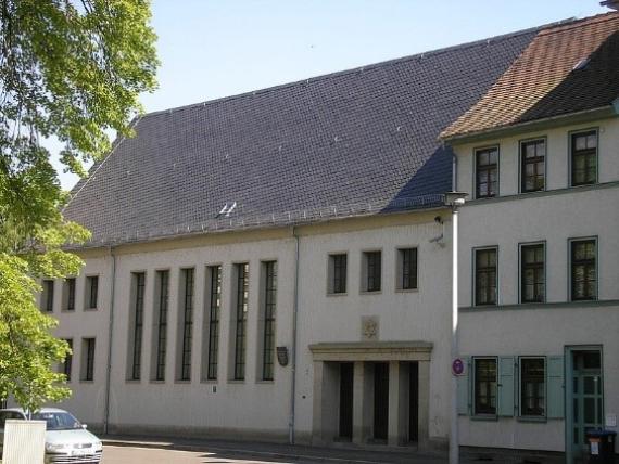 A three-storey house with a steep tiled roof. The entrance has columns. A golden Star of David hangs above the entrance.