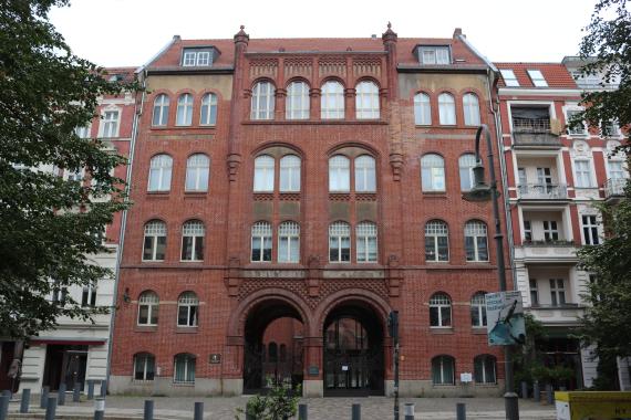 Frontansicht auf rotes Backsteinhaus (Vorderhaus). Durch die Eingänge sieht man im hinteren Bereich die Synagoge