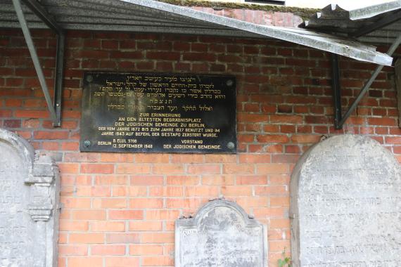 Memorial plaque on brick wall, gravestones next to it