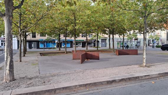 Auf dem Bild ist der ehemalige Standort der Synagoge zu sehen. Der Umriss der ehemaligen Synagoge wird durch Stufen und Plateaus sichtbar. Im Vordergrund liegen bronzefarbene Stahlwinkelstücke.