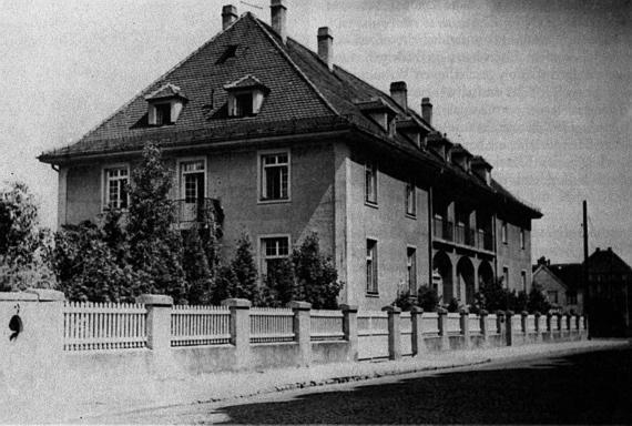 Side view of a detached house with a small fence in front of it. Black and white image.