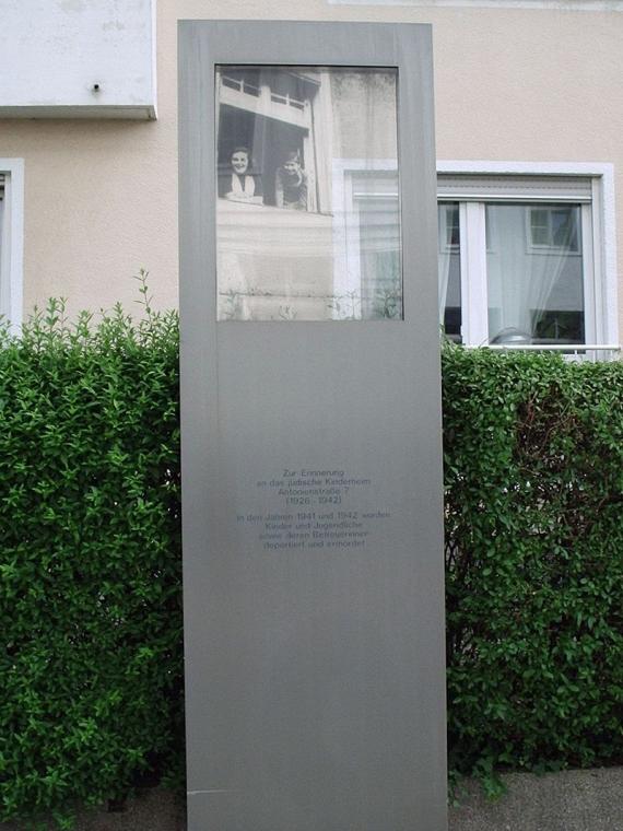 Graue Stele mit Aufschrift und einem Fenster mit Bildaufdruck.