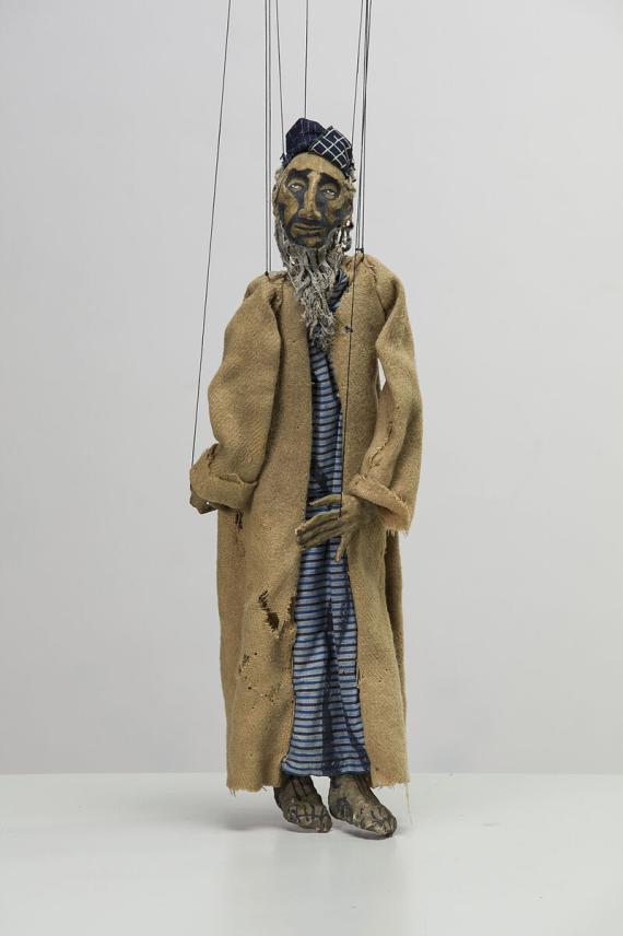 Picture of a marionette. It represents an older man with a long beard and simple clothes.