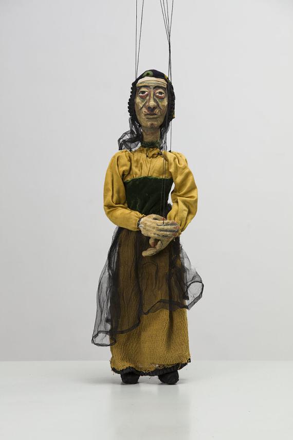 Image of a marionette. She represents an older woman in simple clothing.